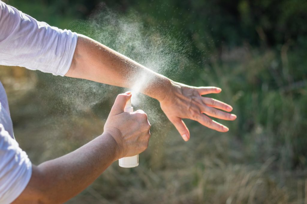 Person sprüht Anti-Mücken-Mittel auf Hand und Arm zum Schutz vor Mückenstichen.