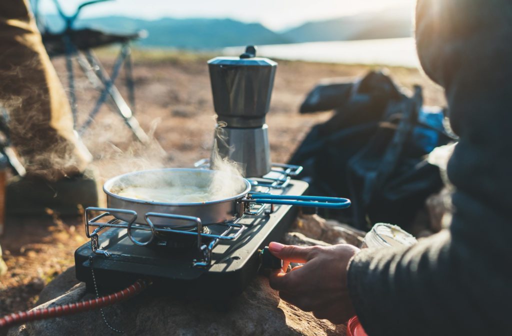 Mann beim Kochen beim Camping, Zubereitung einer Mahlzeit auf einem tragbaren Campingkocher