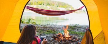 Frau liegt entspannt im Zelt und blickt durch die offene Zeltöffnung hinaus auf einen sonnigen Tag in der Natur.