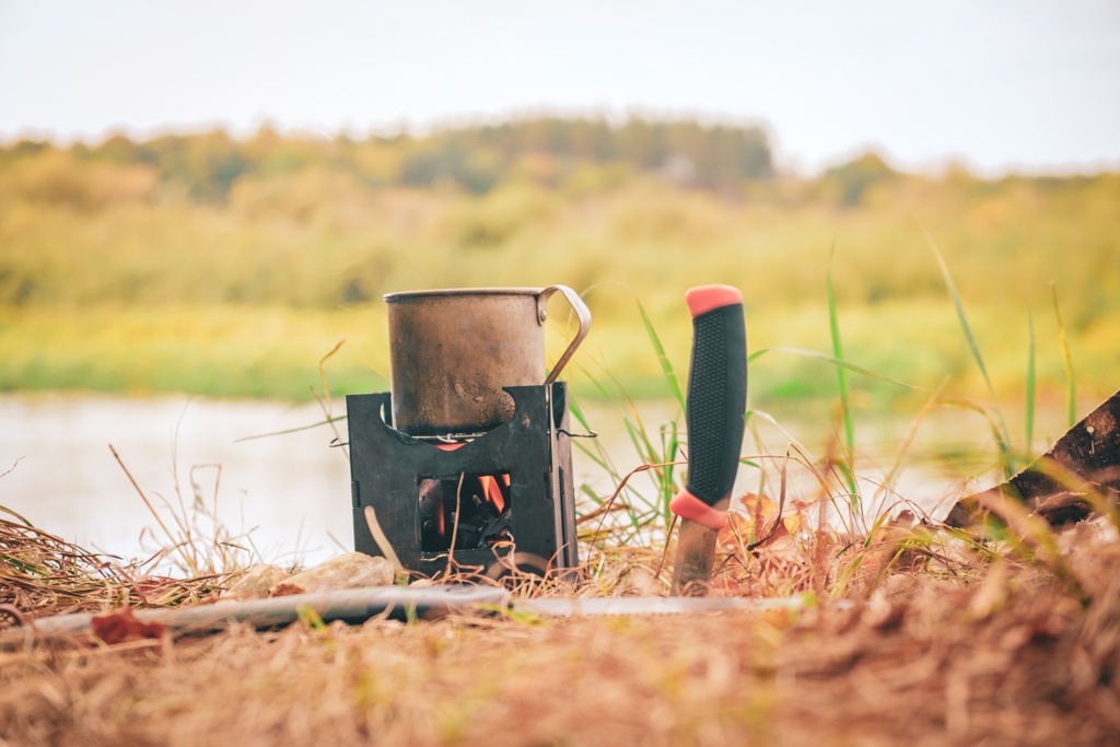 Lekki piecyk Pocket Stove z gotującym się garnkiem, otoczony zielonym mchem i suchymi liśćmi, ustawiony na miękkim podłożu w lesie