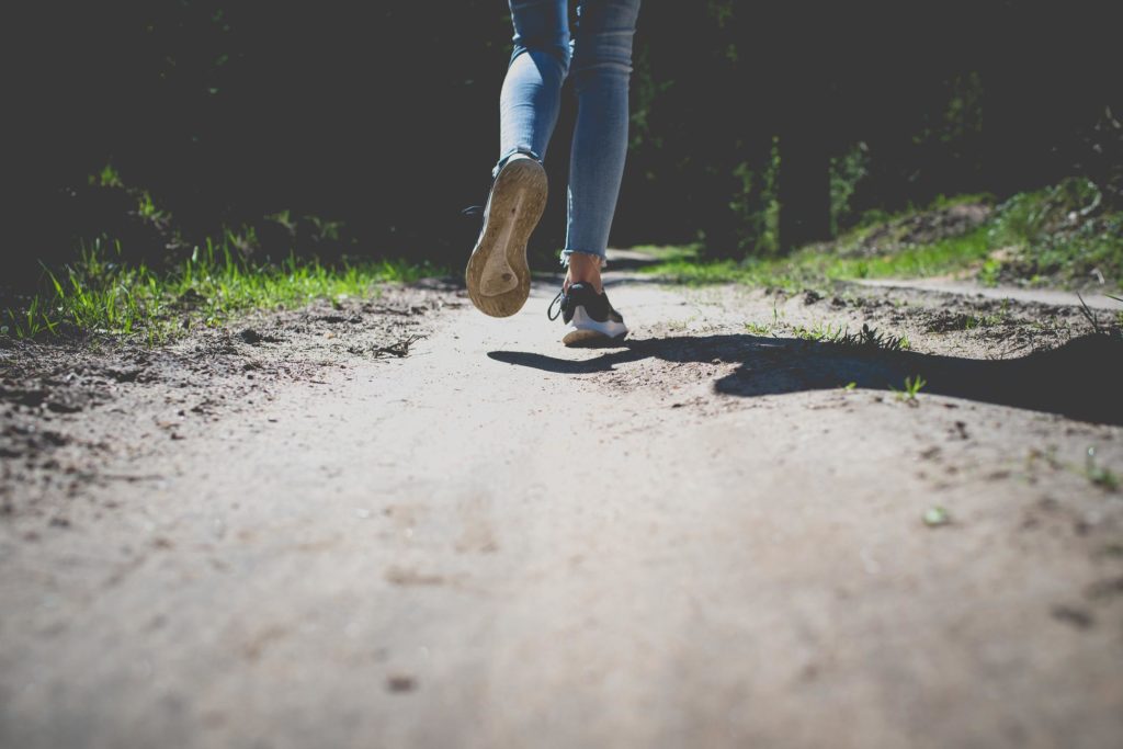 Läuferin joggt durch den Wald, Fokus auf ihre Schuhe.