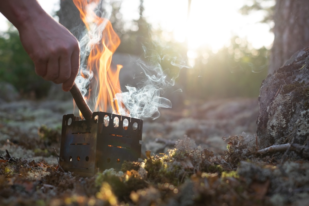 Osoba przygotowująca posiłek na piecyku Pocket Stove w środku lasu, z widoczną patelnią z jedzeniem oraz turystycznymi akcesoriami w tle.