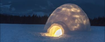 Ein beleuchtetes Iglu bei Nacht in einer verschneiten Landschaft, das Wärme und Geborgenheit im Winter bietet.