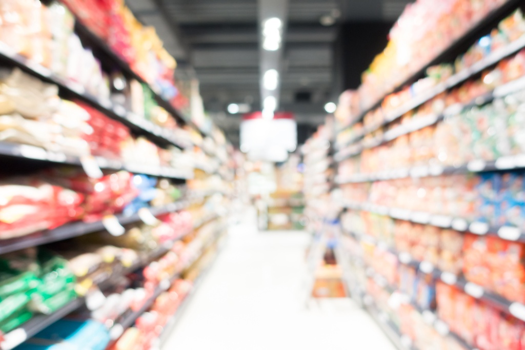 Unscharfe Ansicht eines langen Supermarktgangs mit dicht befüllten Regalen auf beiden Seiten.