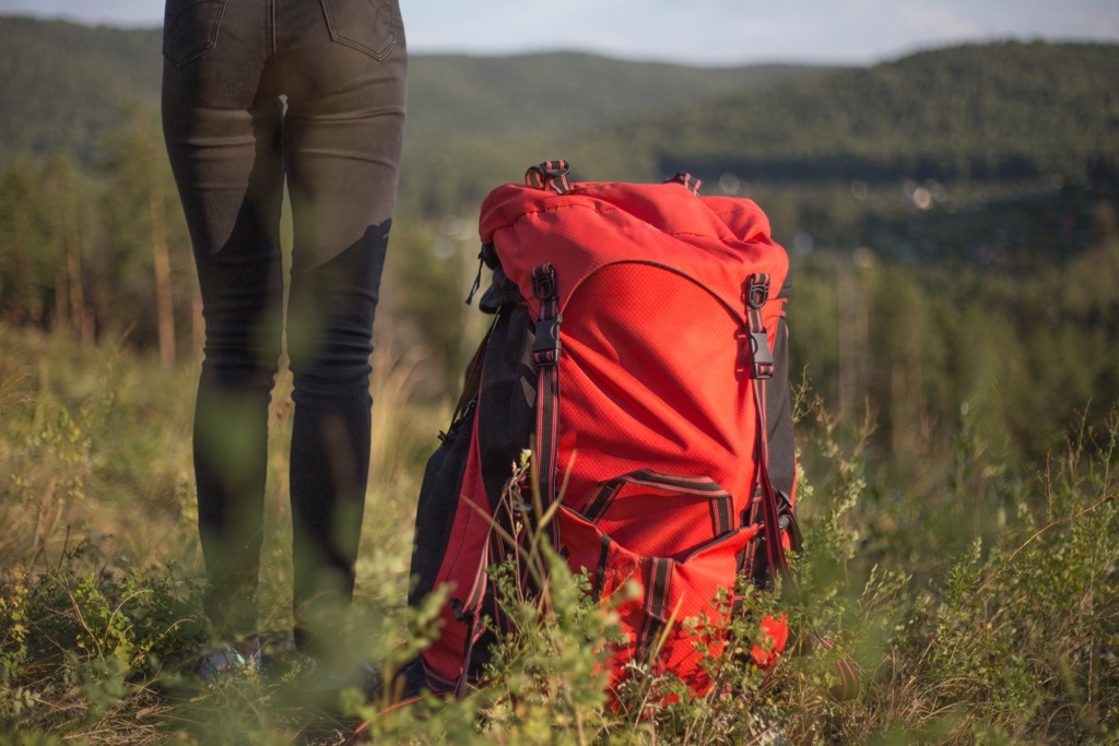 Ein roter Fluchtrucksack auf einer Wiese in den Bergen, bereit für Abenteuer oder Notfälle.