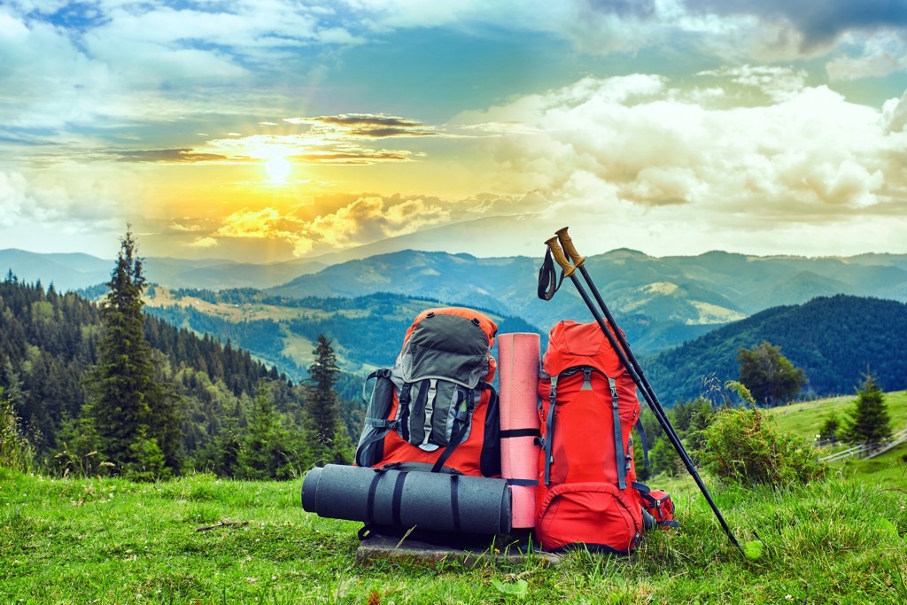 Eine Frau mit rotem Fluchtrucksack steht in der Natur, mit einer malerischen Wald- und Hügelkulisse im Hintergrund.