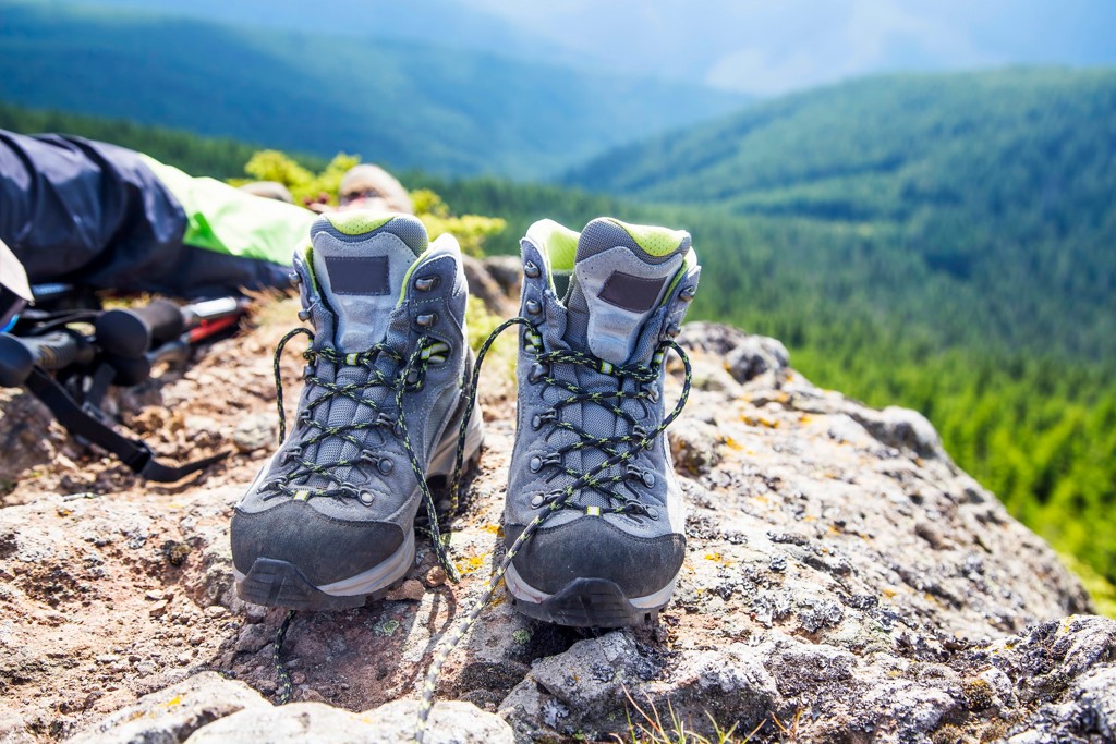 Ein Paar strapazierfähige Trekkingstiefel steht auf einem Felsen mit einer atemberaubenden Aussicht auf bewaldete Berge.