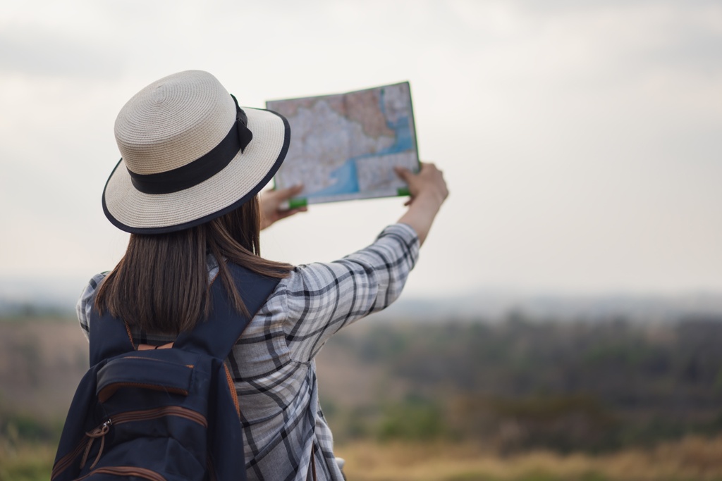 ine Person mit Hut und Rucksack hält eine Karte in der Hand und betrachtet die Landschaft.