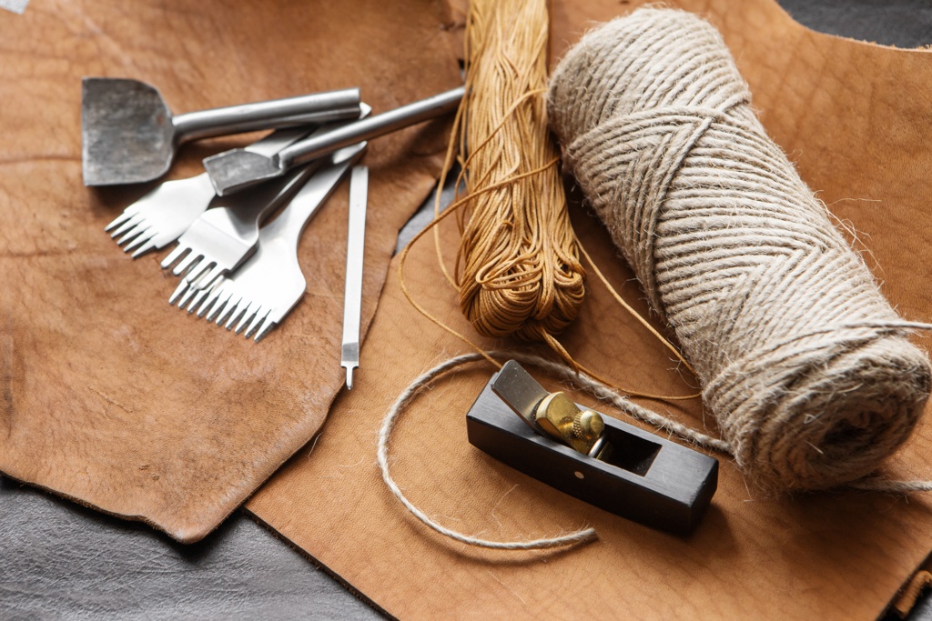 Lederhandwerkswerkzeuge, einschließlich Ahlen, Garn, Leinenfaden und Ledermaterial, arrangiert für Bastel- oder Reparaturarbeiten.